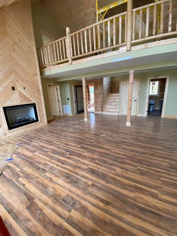 Spacious interior with wood flooring, fireplace, and a second-floor balcony. Green walls, and light-colored doors.