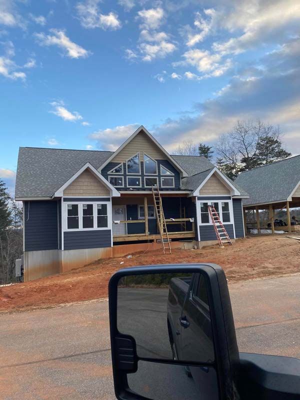 Newly constructed blue house with white trim, tan accents, and large windows, on a hillside under a cloudy sky.