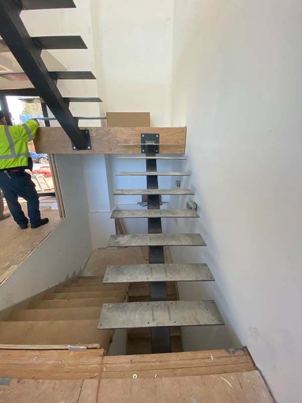 Staircase under construction: Wooden steps and support structure, metal beam. Construction worker in safety vest.