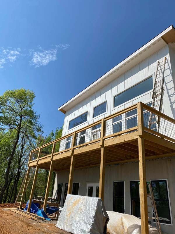 Two-story modern house under construction with a large wooden deck and a clear blue sky.