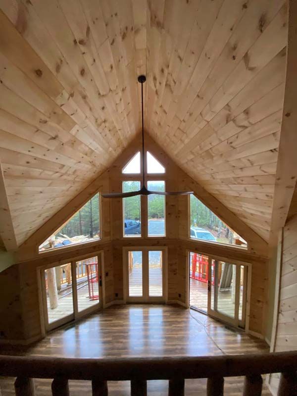Wooden interior with large windows, vaulted ceiling, and a ceiling fan.