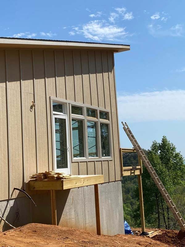 Exterior of house under construction with light brown siding, windows, and a ladder against the deck; blue sky.