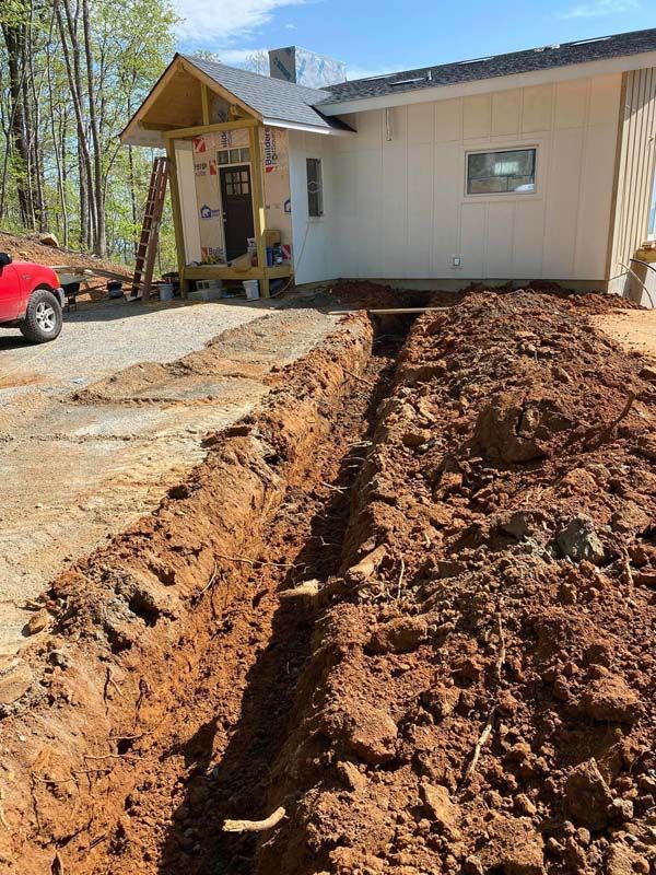 A deep trench dug near a newly built white house with a porch, red soil visible.