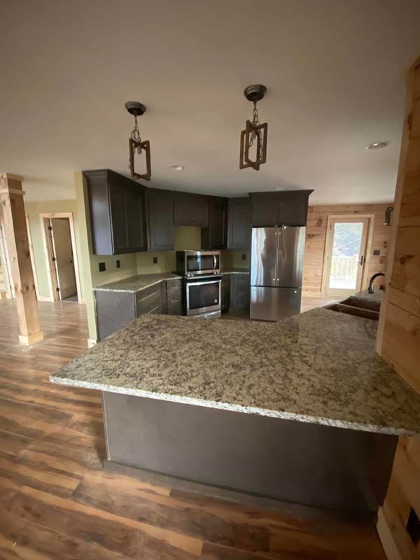 Modern kitchen with brown cabinets, granite countertop island, stainless steel appliances, and wood floor.
