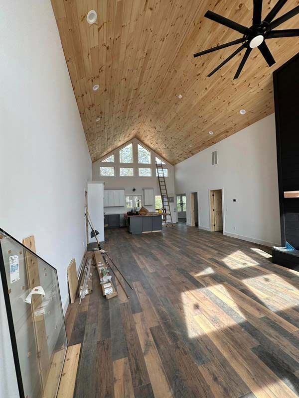 Interior view of a spacious room with wood floors and ceiling, white walls, and a black ceiling fan.