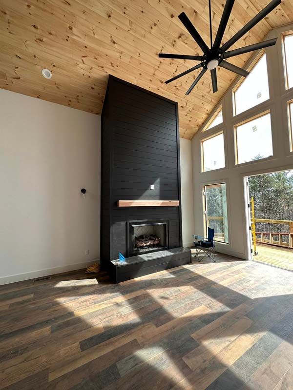 Modern living room with a black fireplace, wood floors, and tall windows.