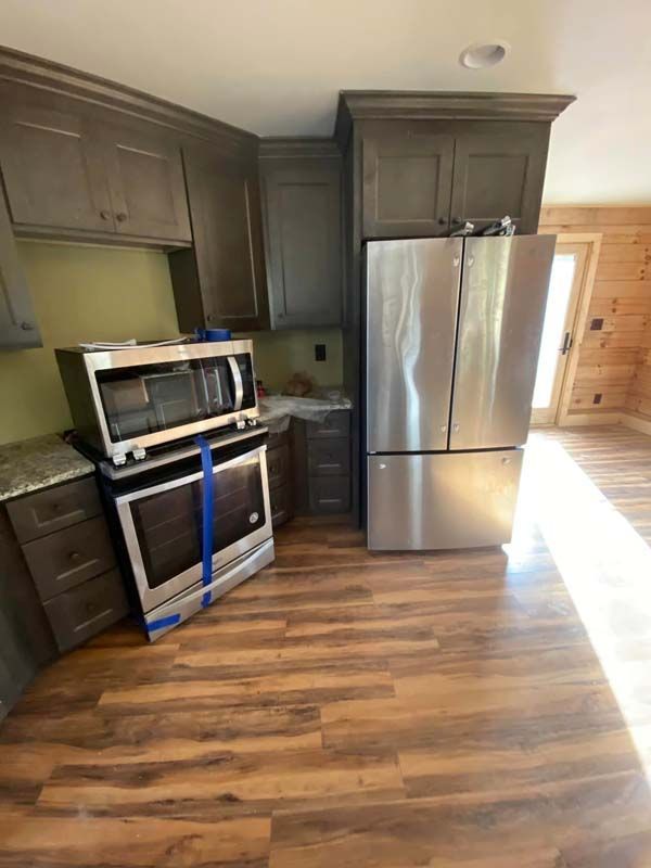 Kitchen with dark cabinets, stainless steel refrigerator, and oven. Microwave sits on top of the oven.