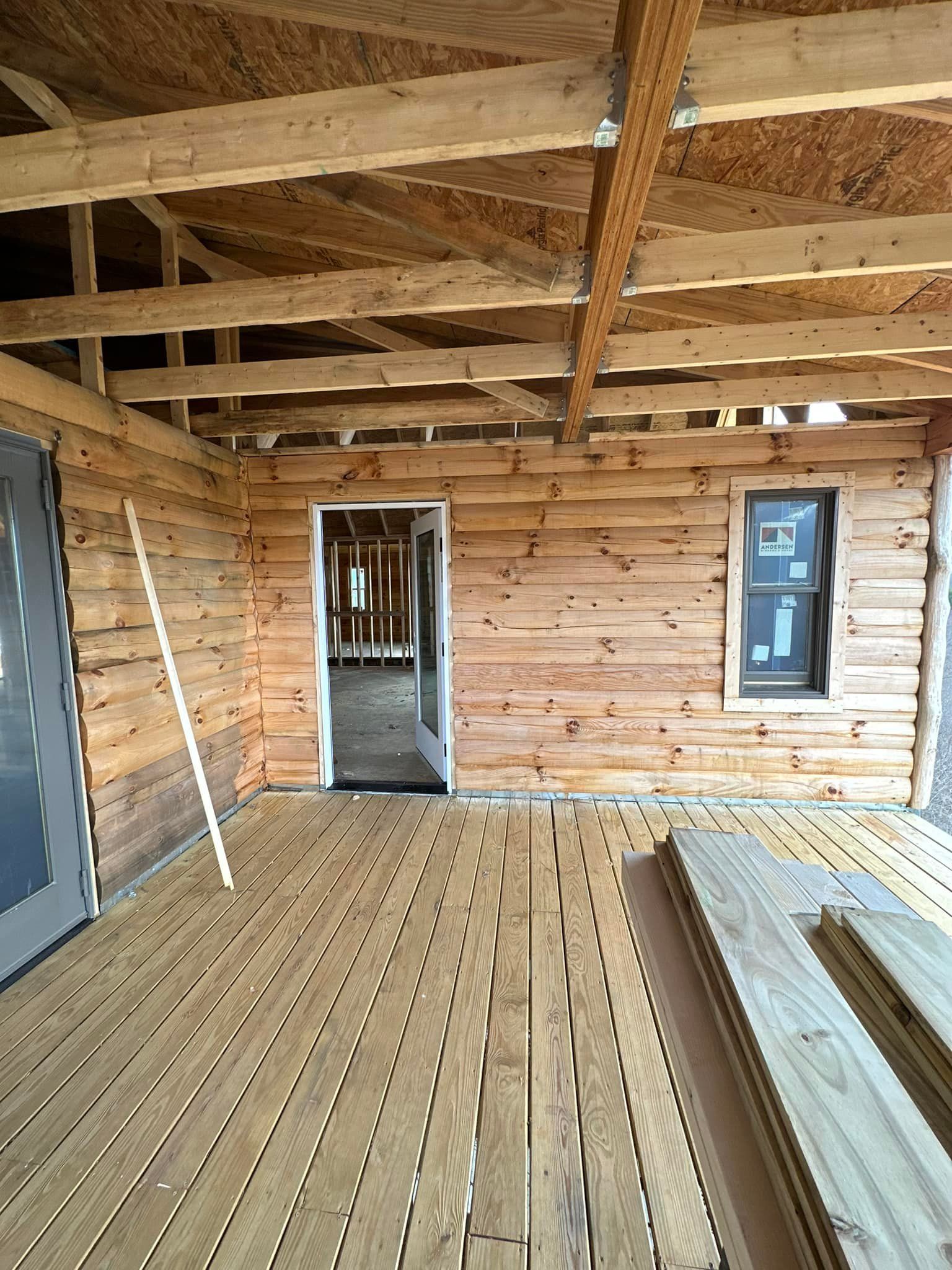 Wood-framed construction, deck, interior, with log siding walls, doorway, window, unfinished.