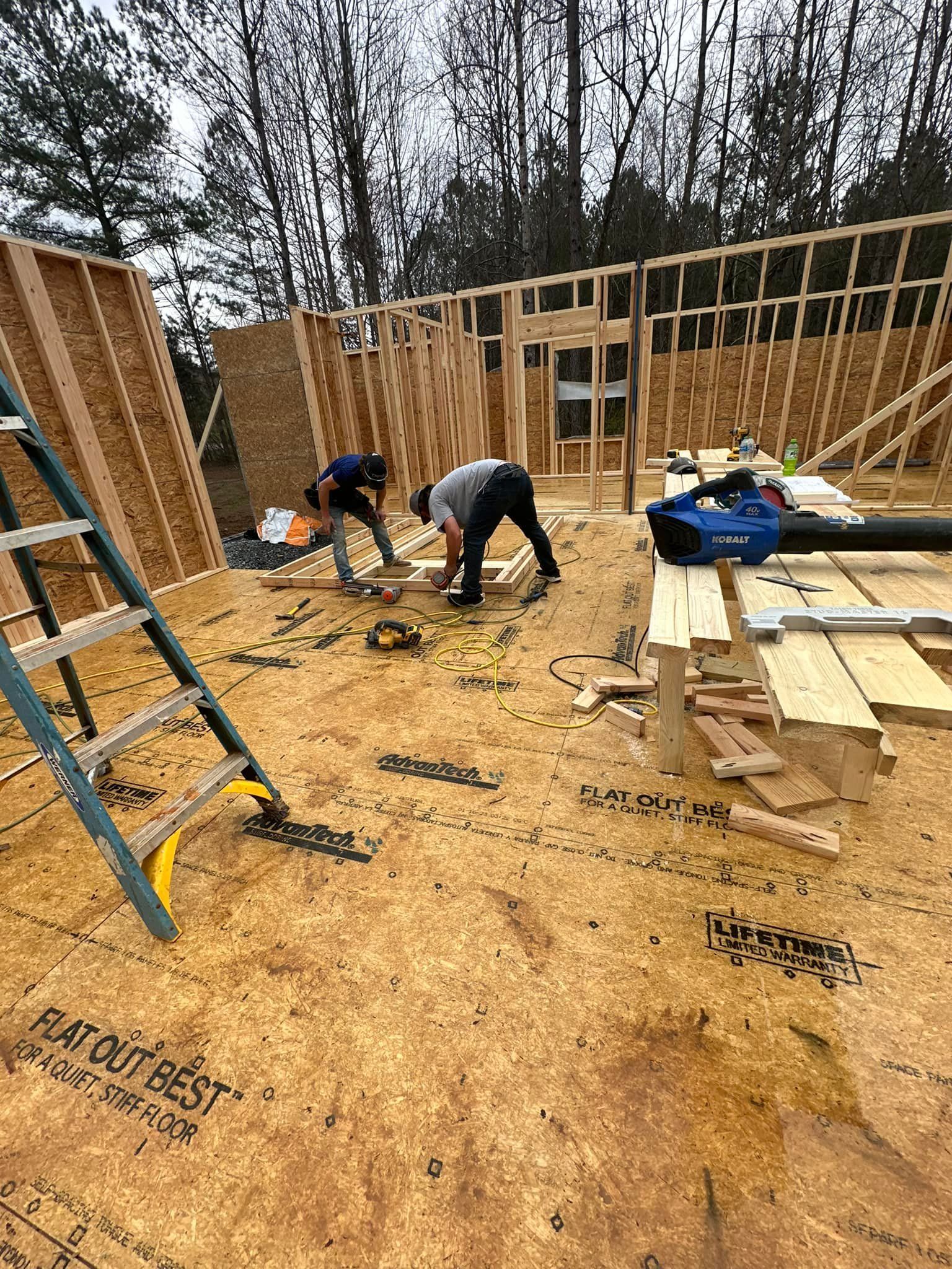 Two construction workers building a wood-framed structure outdoors. One uses a blower.