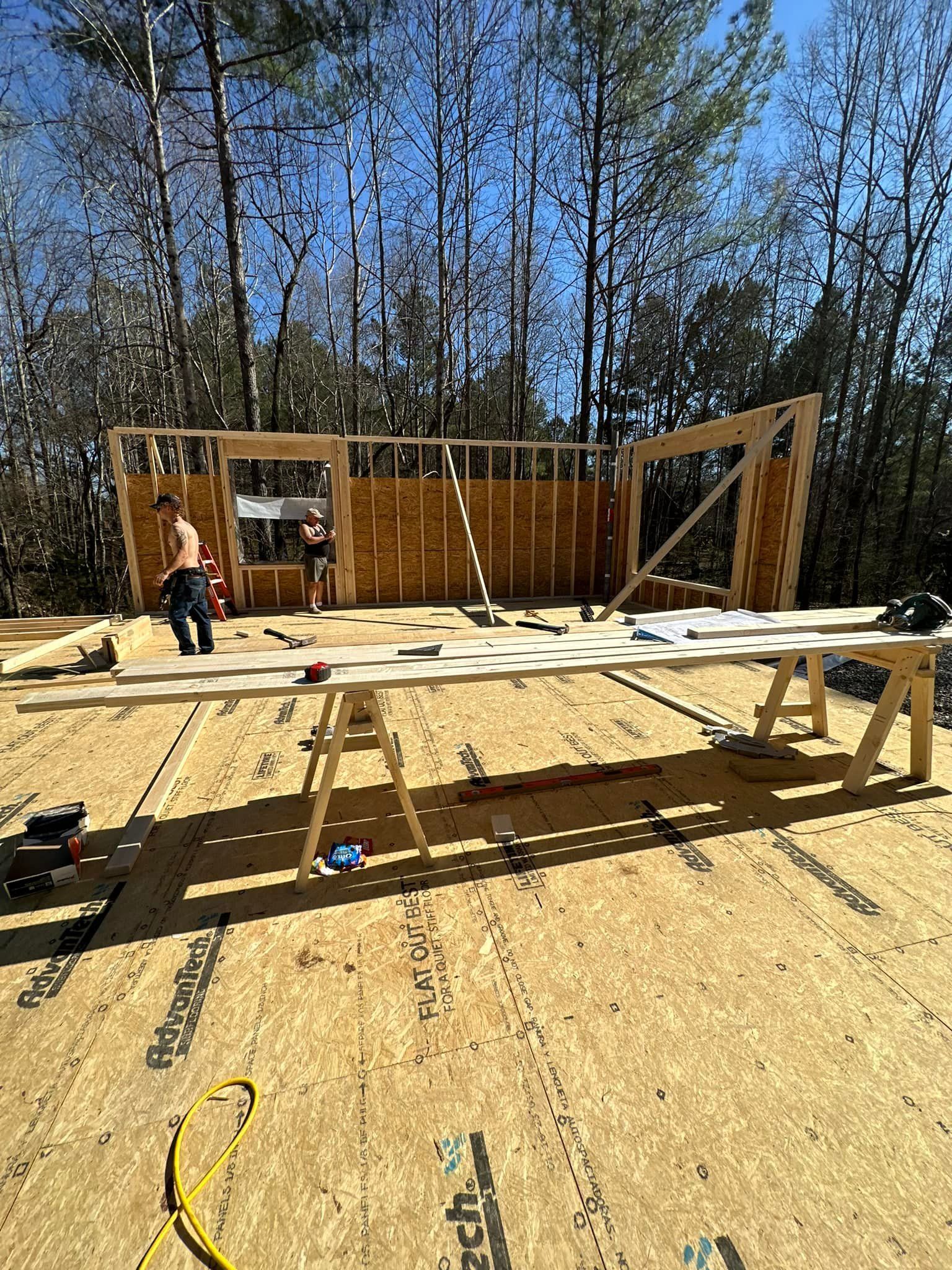 Construction of a building frame with two people working, wood, and a sunny setting.