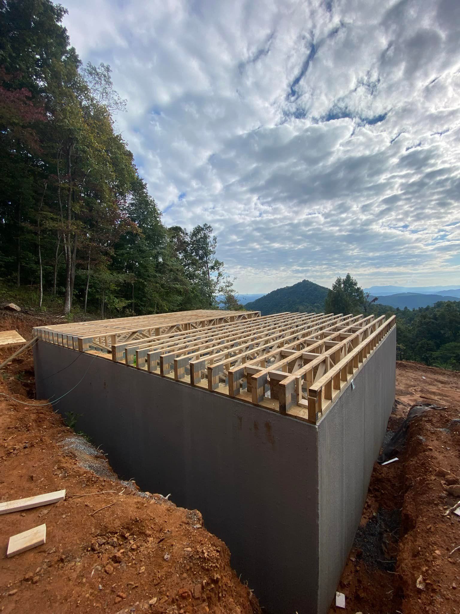 Triangular concrete structure with wooden beams, under construction on a hillside, cloudy sky.