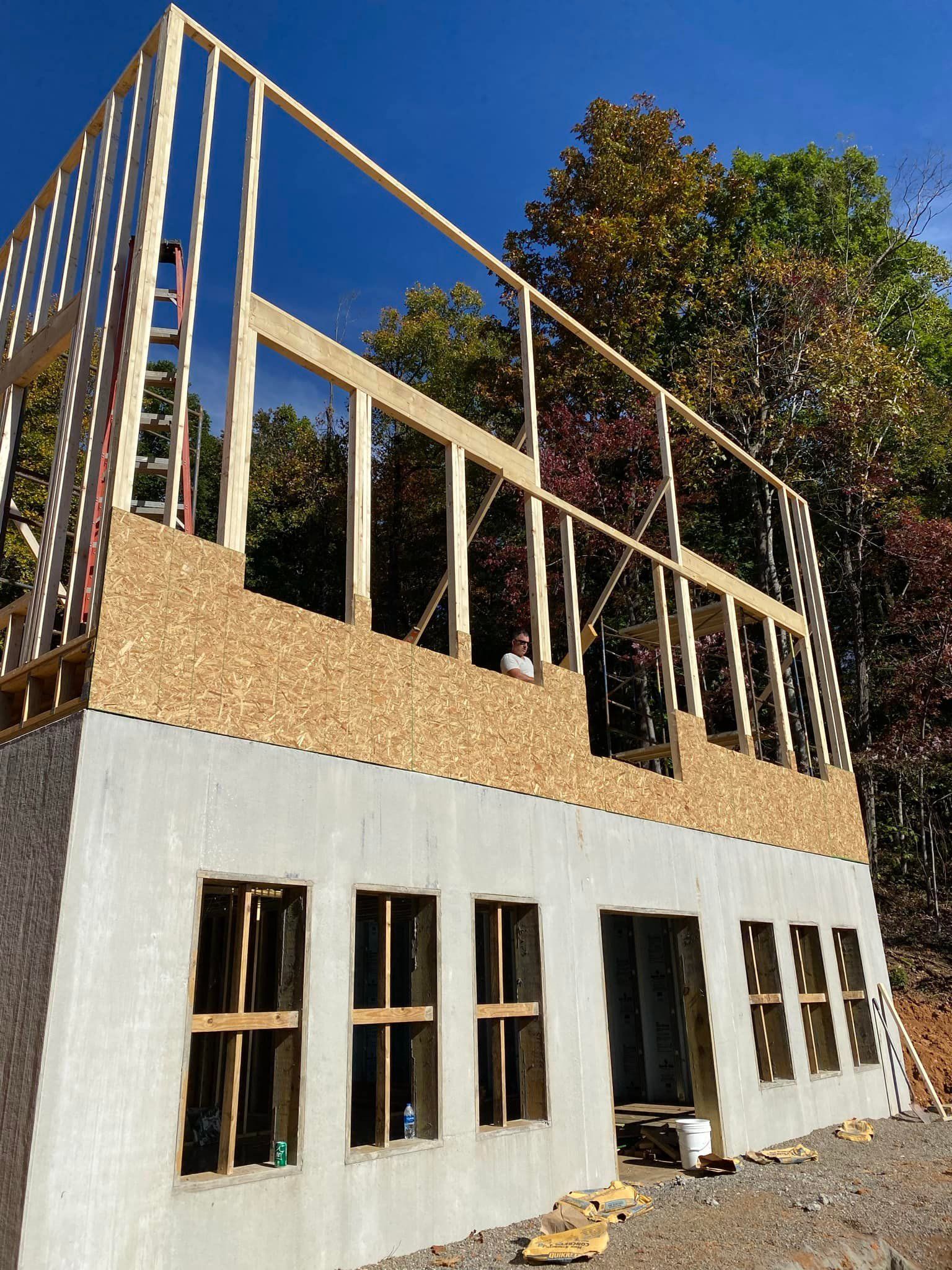 Construction of a two-story building with wood framing and concrete walls; clear blue sky.