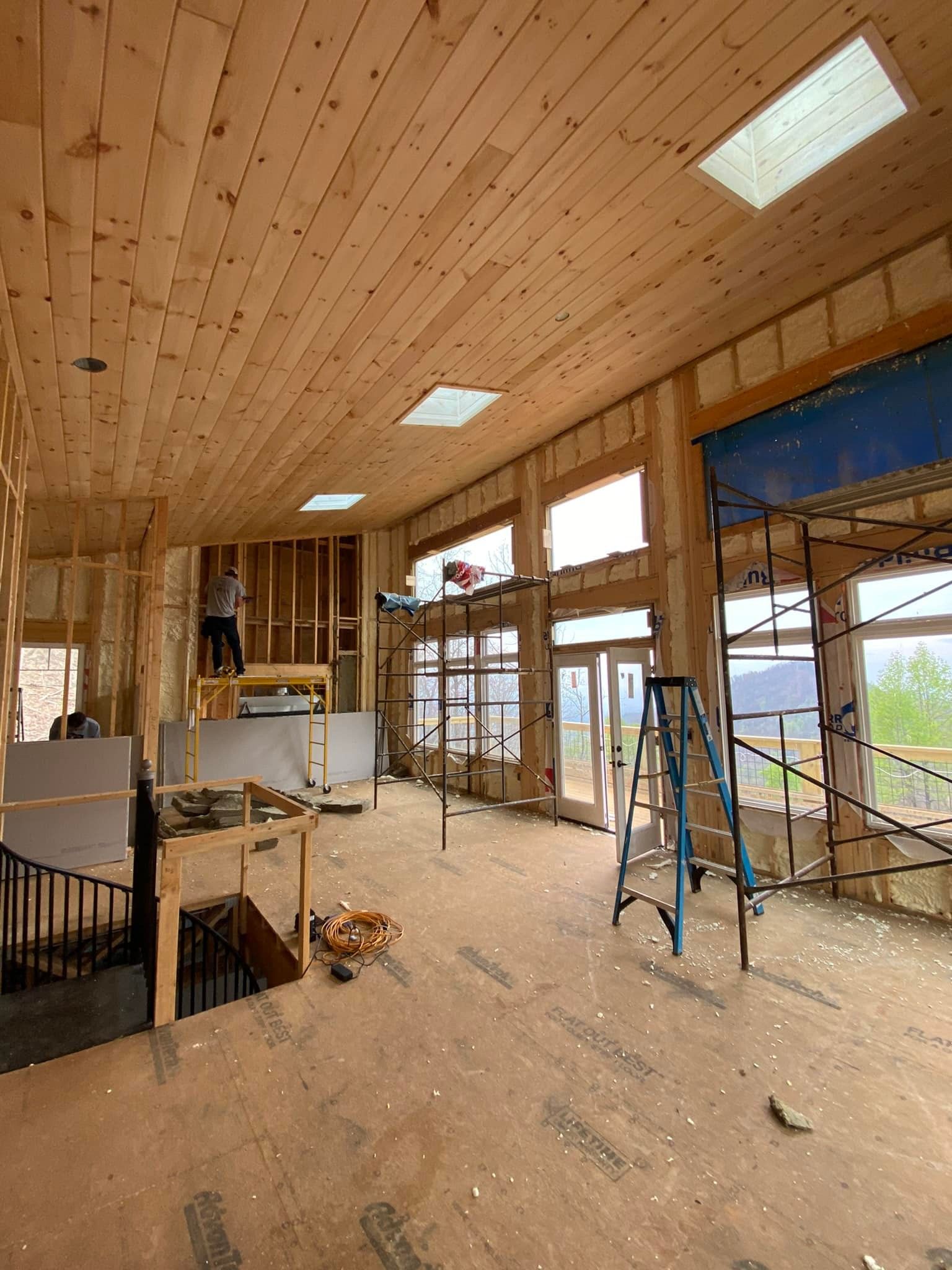 Interior of a house under construction; wooden walls and ceiling, large windows, scaffolding, and tools.