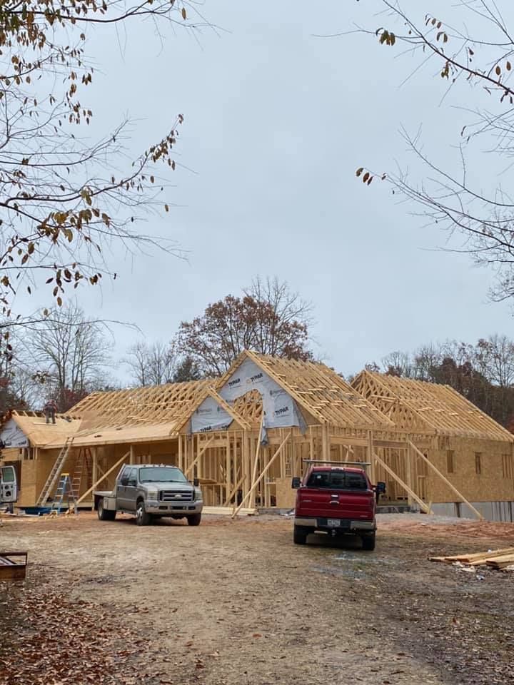 House under construction with exposed wooden frame; two pickup trucks parked in front.