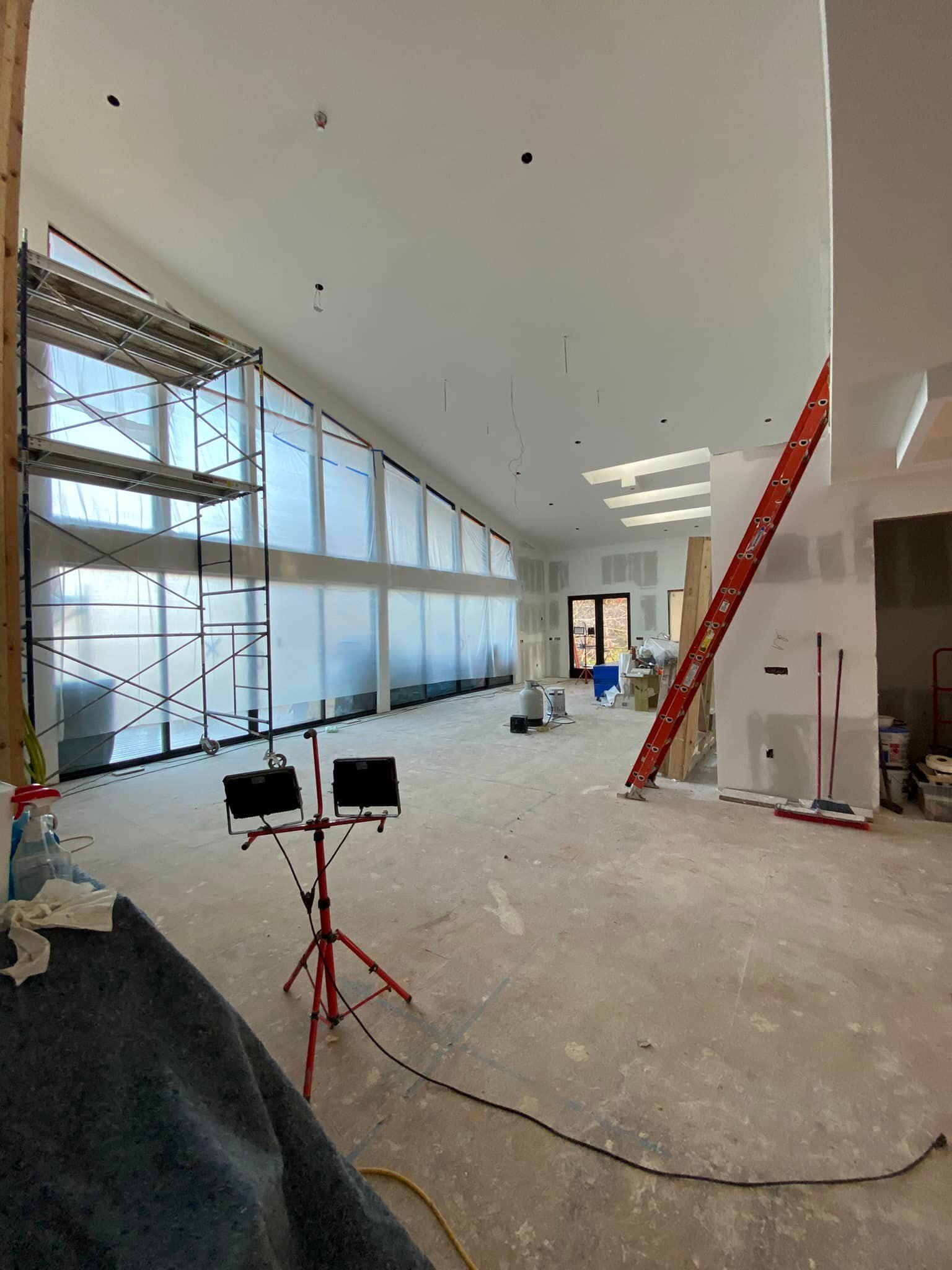 Interior view of a building under construction, featuring tall windows, scaffolding, and a ladder.