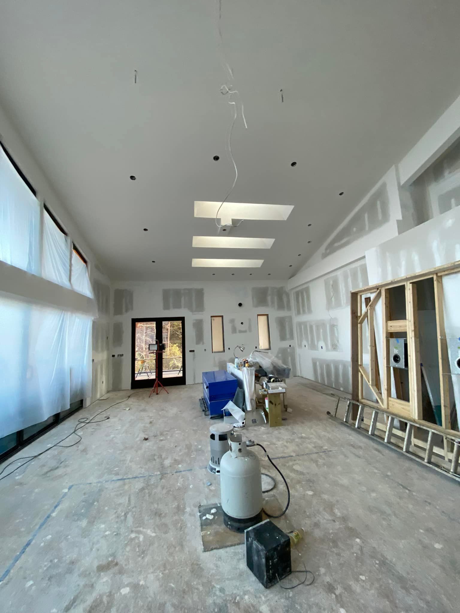 Interior construction: room with drywall on walls and ceiling, uncovered floor, and large windows.