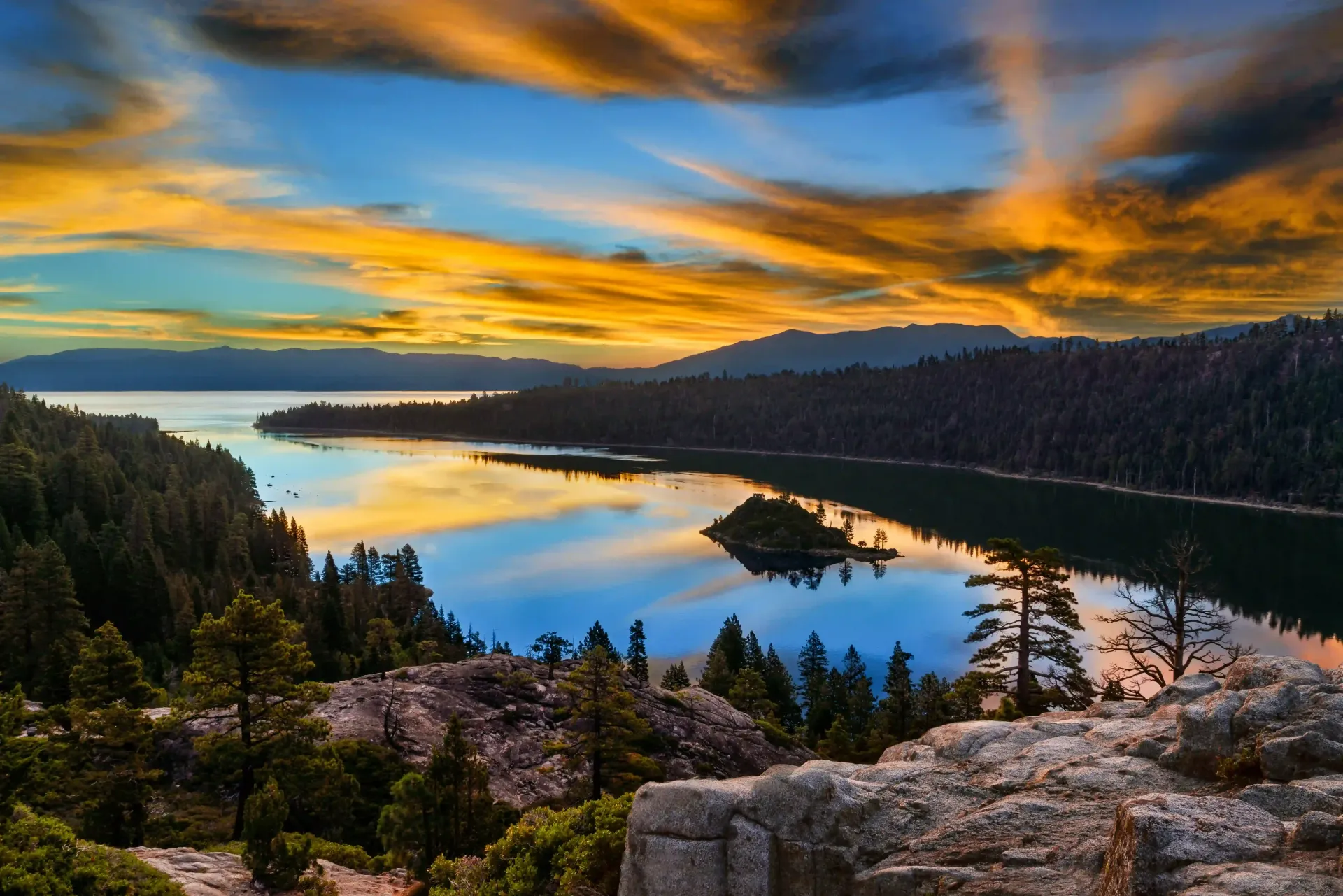 Emerald Bay at Lake Tahoe during a vibrant golden sunset with a small island in the calm, reflective water.