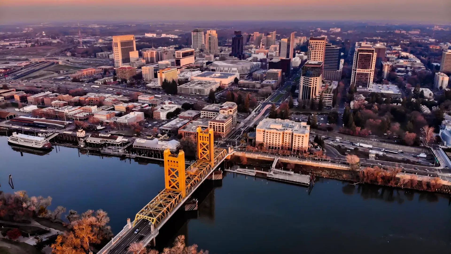Aerial view of Sacramento’s yellow Tower Bridge spanning the Sacramento River at sunset, with the city skyline behind.