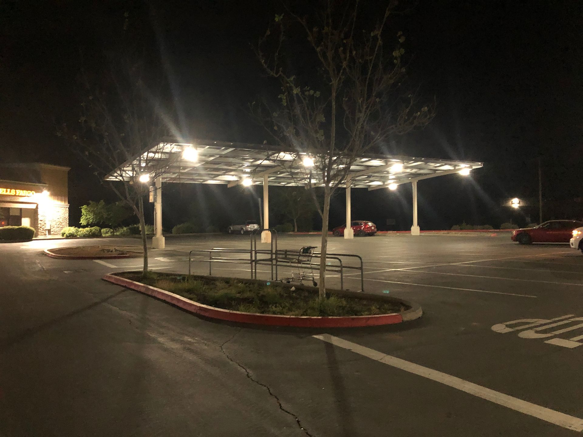 A parking lot at night featuring a large solar panel canopy structure illuminated by bright overhead lights.
