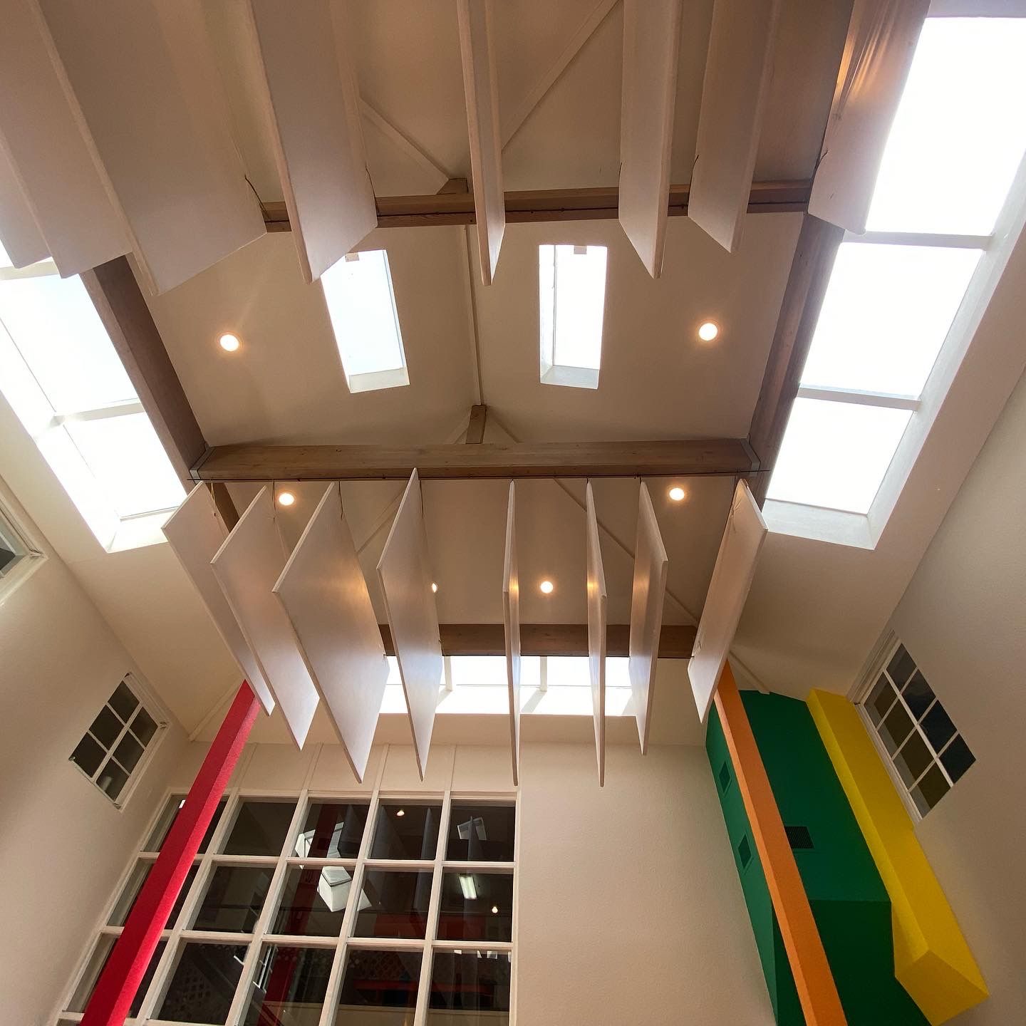 A low-angle view of a high ceiling with skylights, wooden beams, and white acoustic panels hanging vertically.