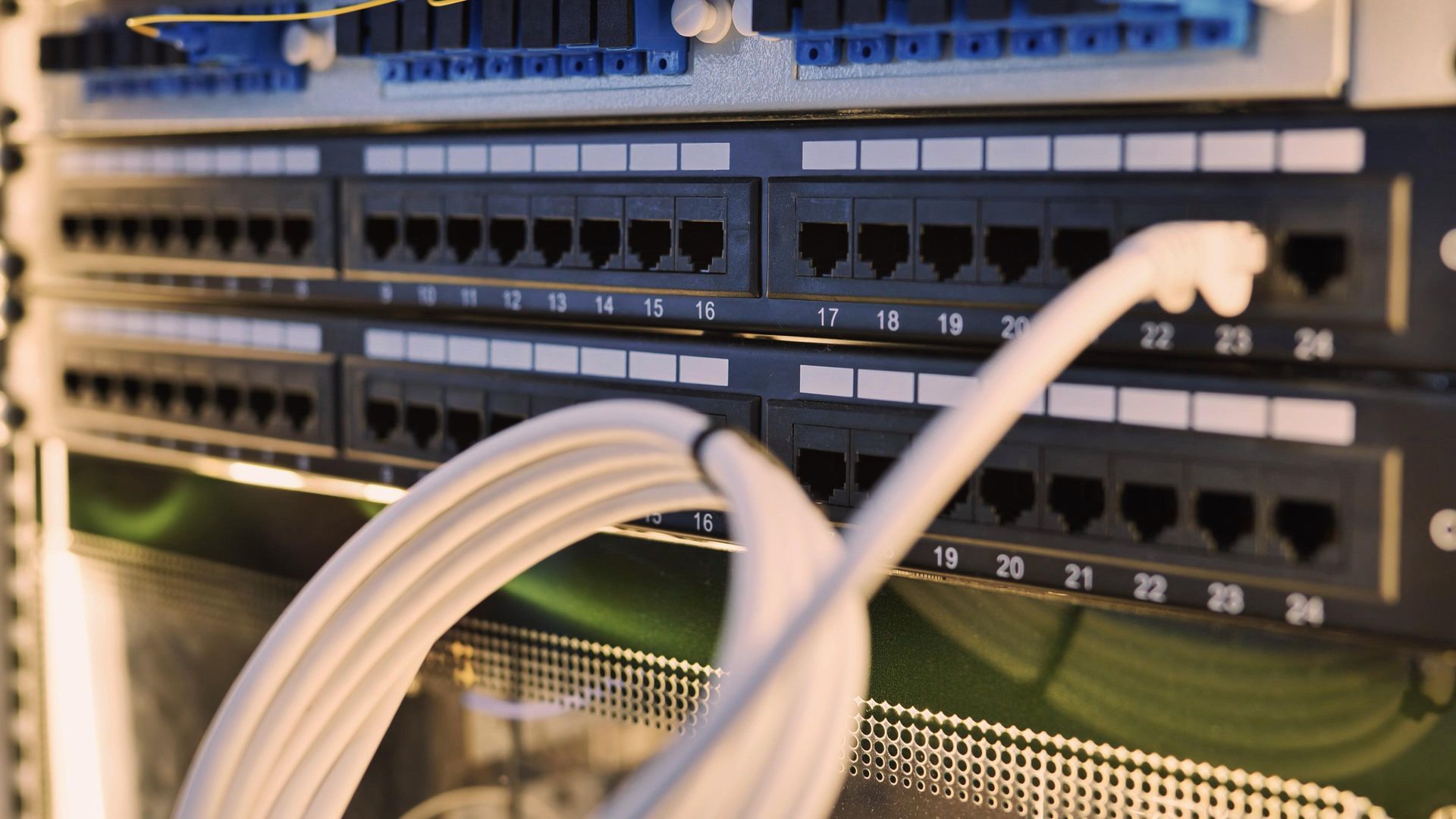Close-up of a white Ethernet cable plugged into port 23 of a black network patch panel in a server rack.