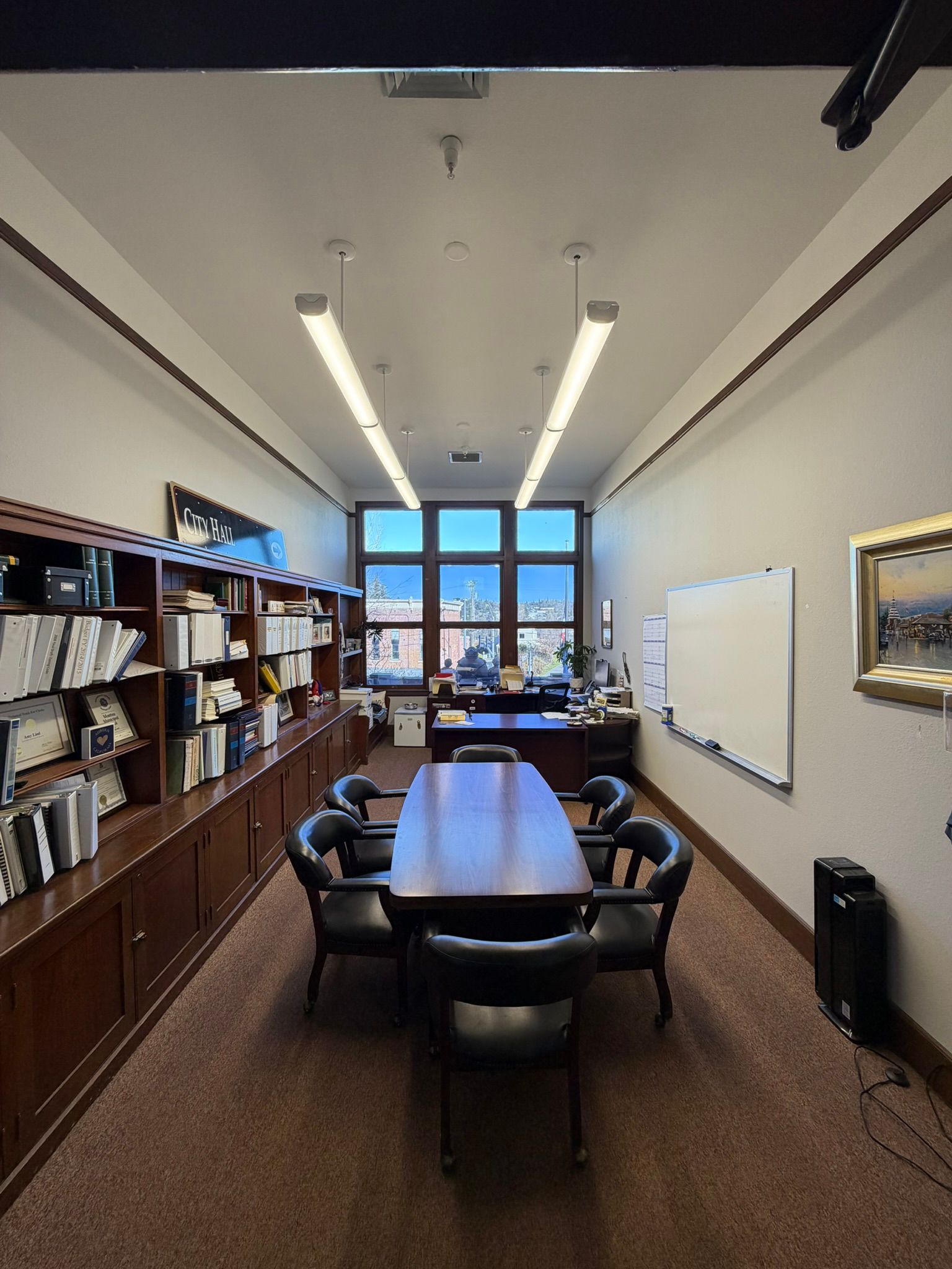 A long conference room featuring a dark wood table with six chairs, built-in wooden bookshelves, and a whiteboard.
