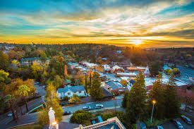 A scenic aerial view of a town nestled among trees at sunset, with golden light illuminating the horizon.