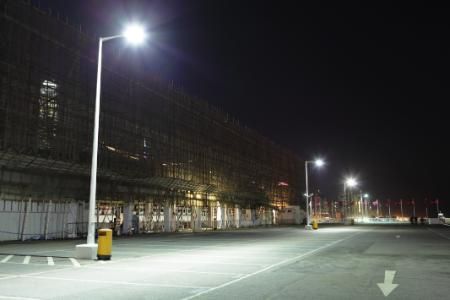 A well-lit parking lot at night, featuring a row of streetlights illuminating the asphalt surface near a building.