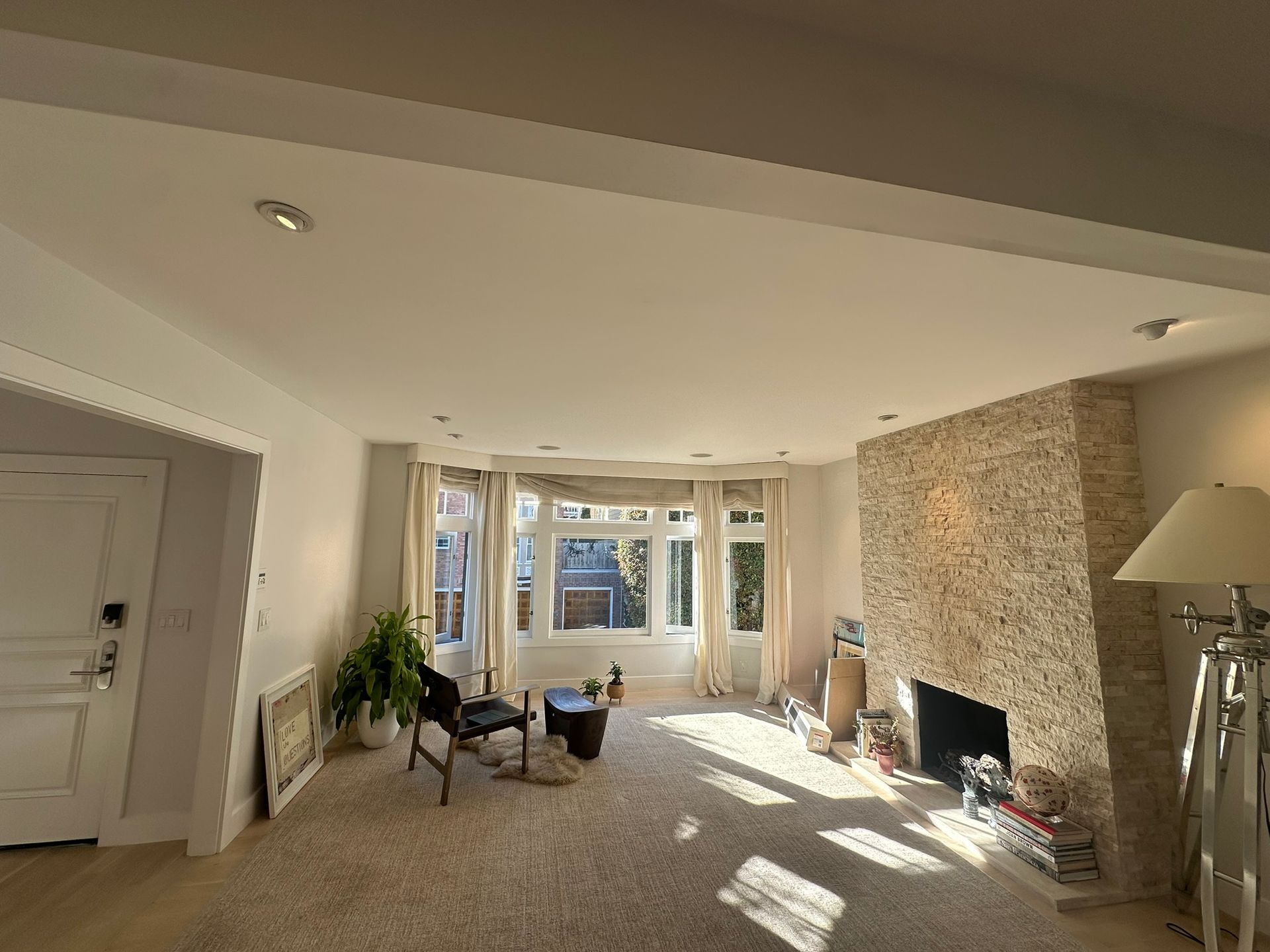 Living room with a stone fireplace, large bay window, neutral carpet, a chair, and recessed lighting.