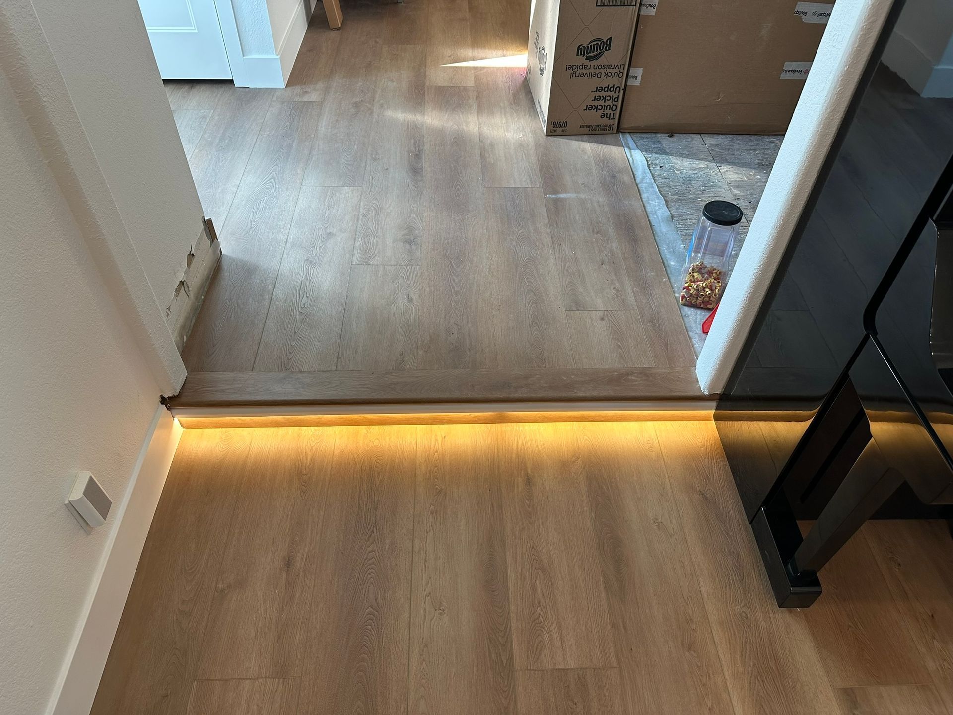 A transition between two wood-floored rooms features a strip of warm under-cabinet LED lighting at the threshold step.