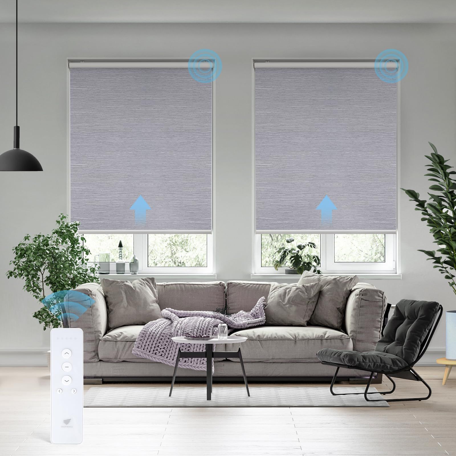 A living room features two light-gray motorized roller shades being operated by a white remote control in the foreground.