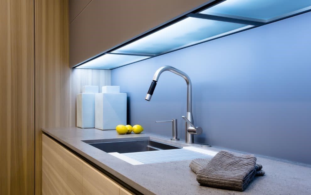 A modern kitchen sink area with a stainless steel faucet, grey countertop, and blue under-cabinet lighting.