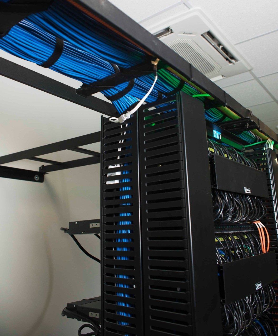 A server rack in a data center, with a dense bundle of blue ethernet cables in overhead trays connected by a ground wire.