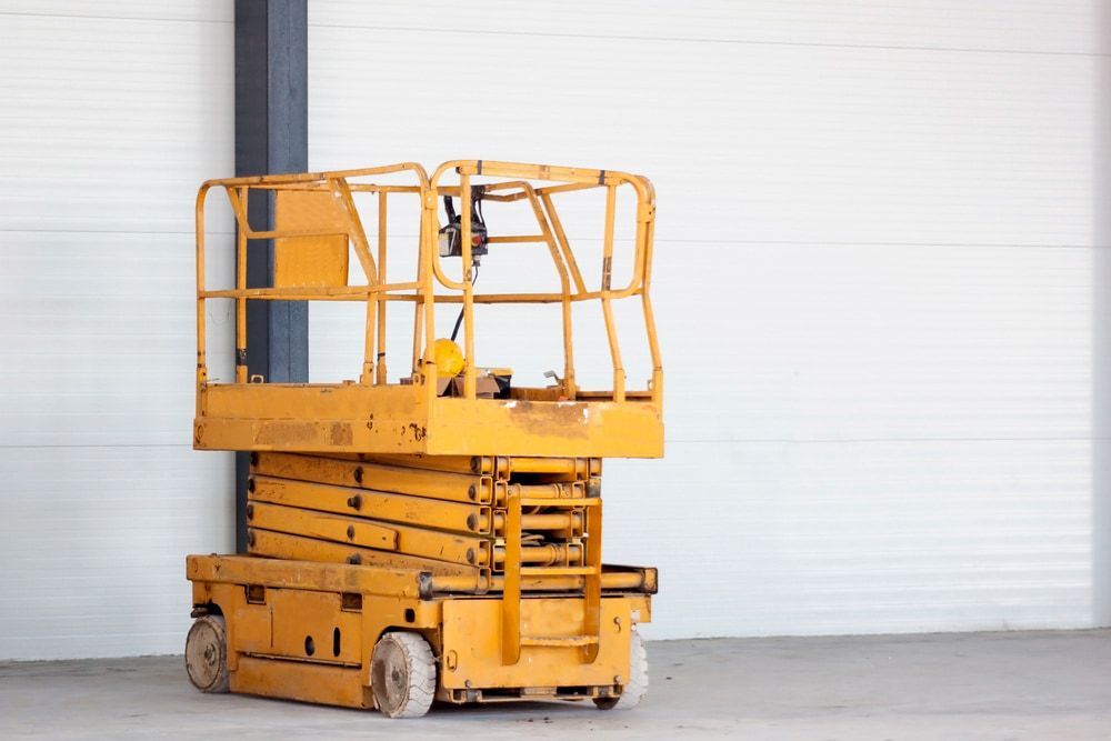 A Yellow Scissor Lift is Parked in Front of a White Wall in a Warehouse — Innisfail Auto Electrics Pty Ltd in Babinda, QLD