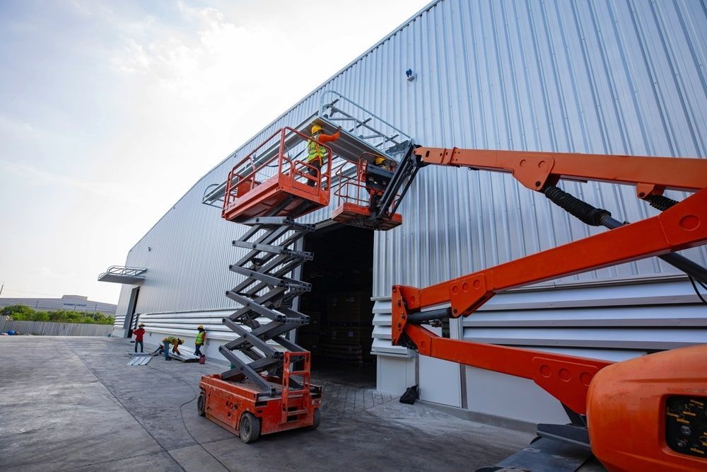 A Man is Standing on a Scissor Lift in Front of a Building — Innisfail Auto Electrics Pty Ltd in Babinda, QLD