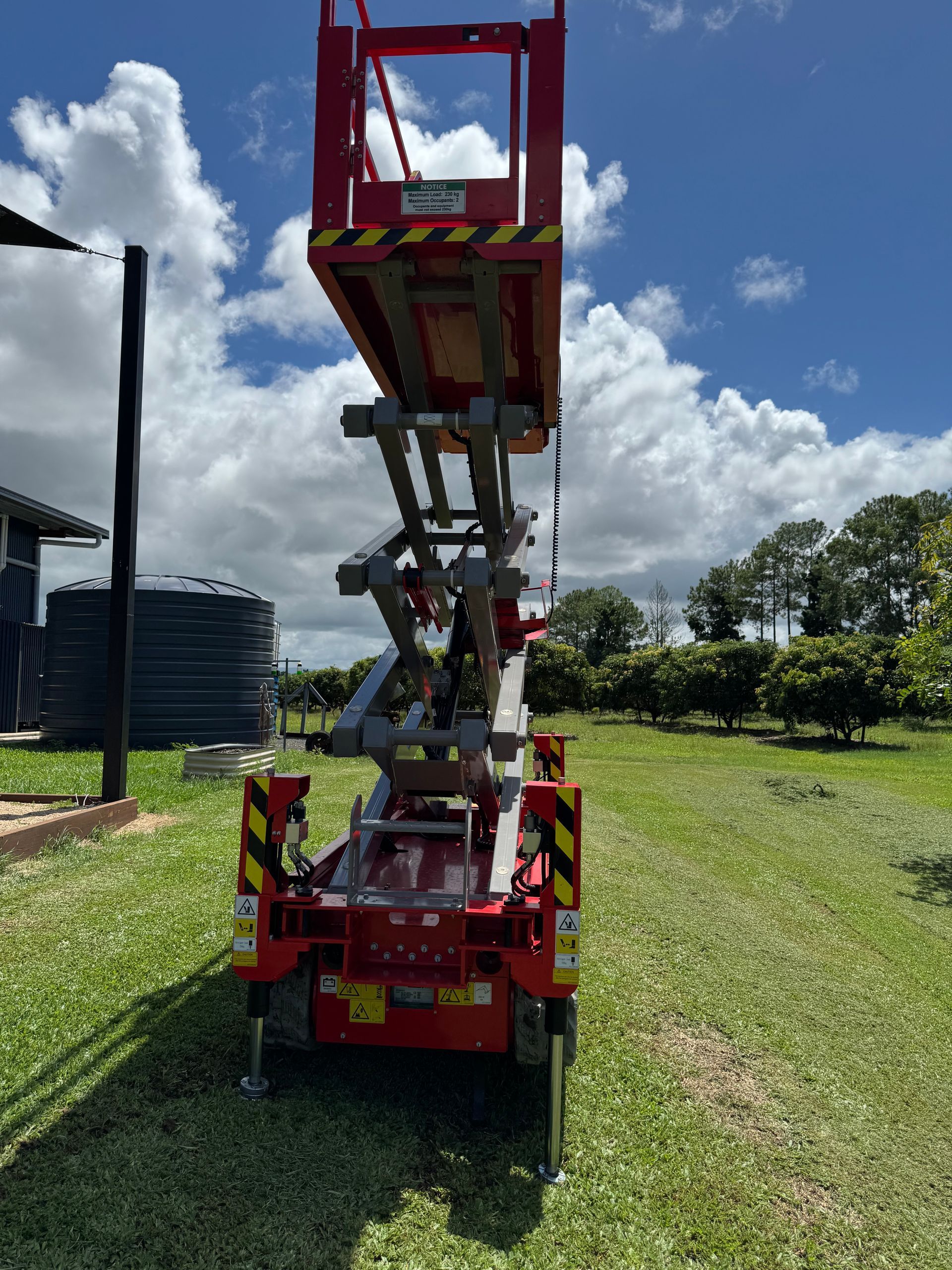 A Red Scissor Lift is Parked On The Grass— Innisfail Auto Electrics Pty Ltd in Mundoo, QLD
