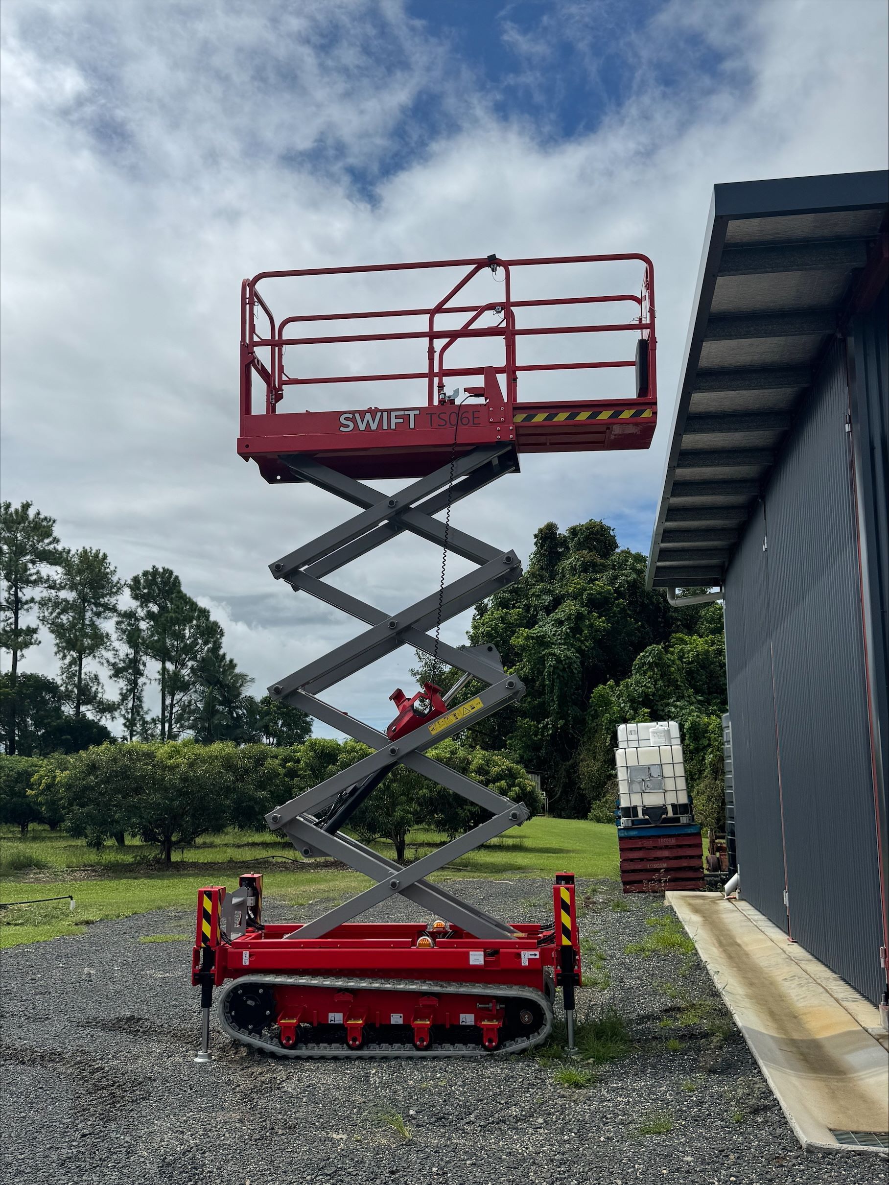 A Red Scissor Lift is Parked in Front of a Building — Innisfail Auto Electrics Pty Ltd in Mundoo, QLD