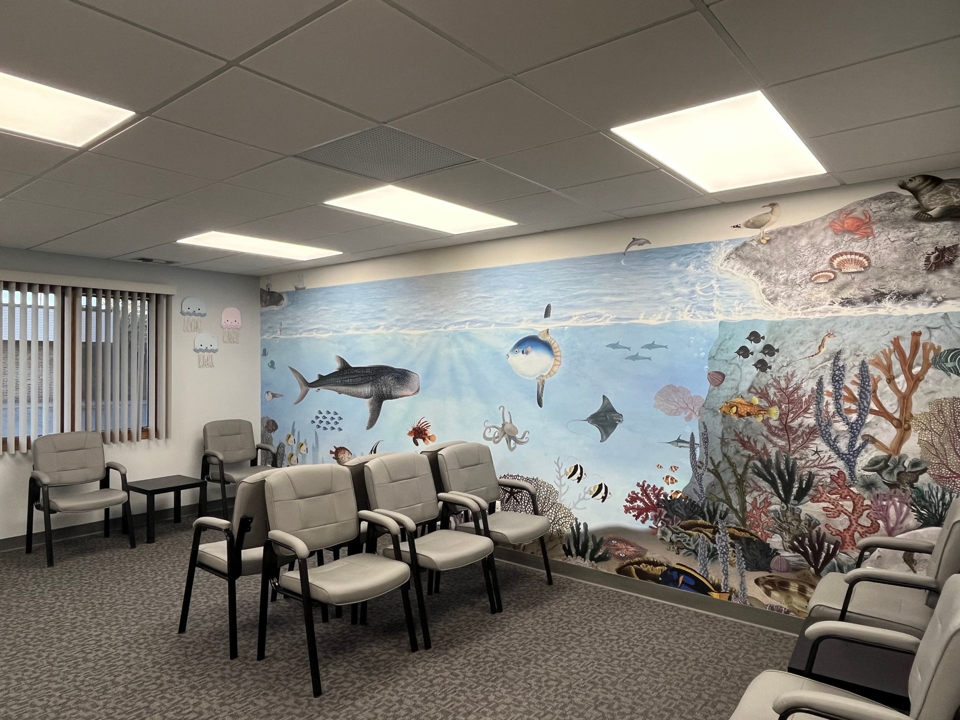 A waiting room with gray chairs and an ocean-themed mural featuring fish, coral, and other marine life.