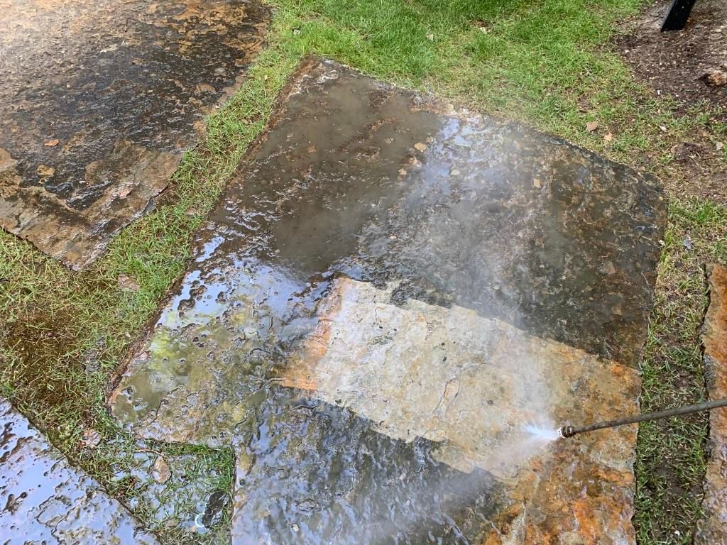 A person is cleaning a concrete walkway with a pressure washer.