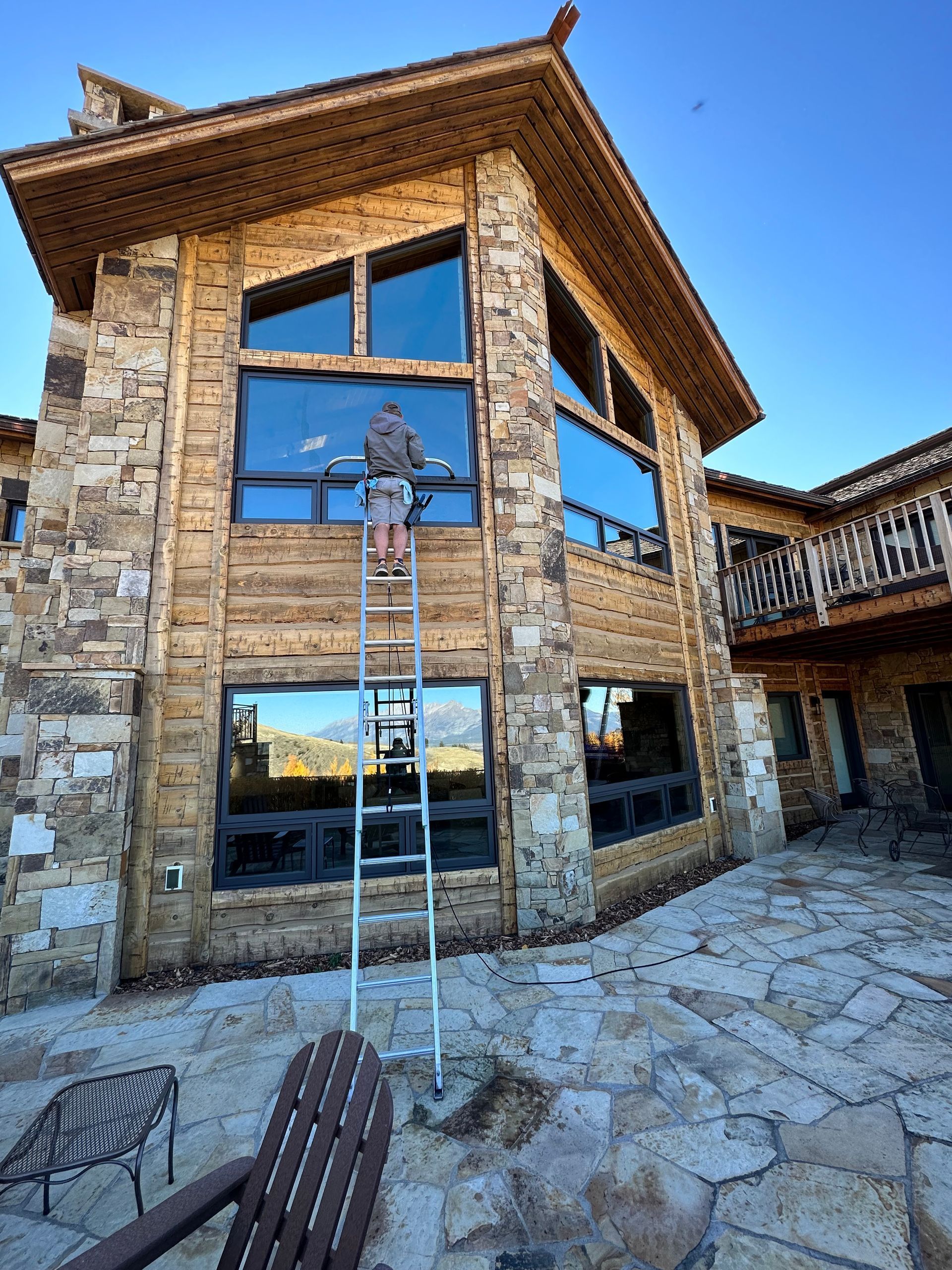 A man on a ladder is cleaning the windows of a large house