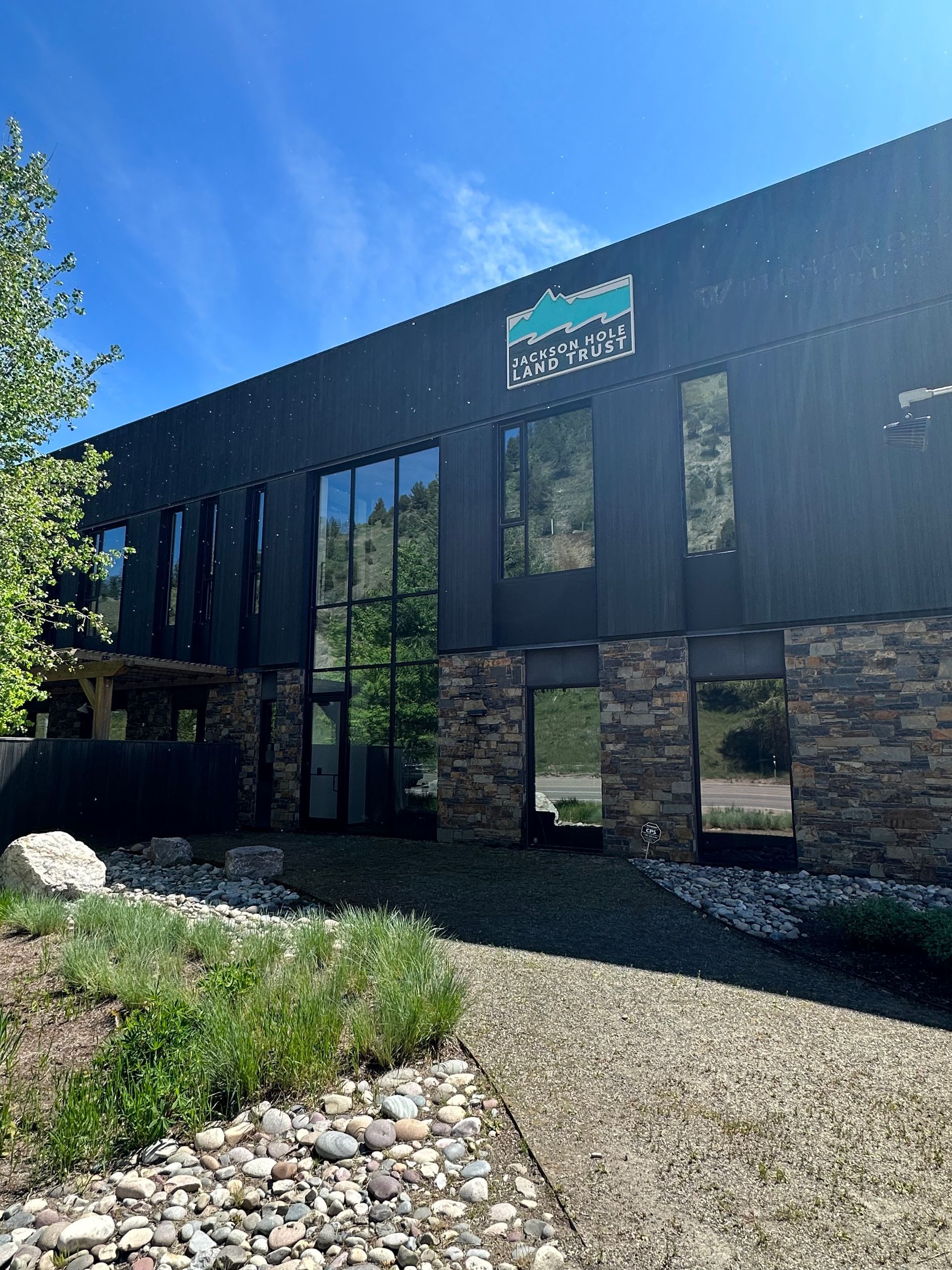 A large black building with a lot of windows is surrounded by rocks and trees.