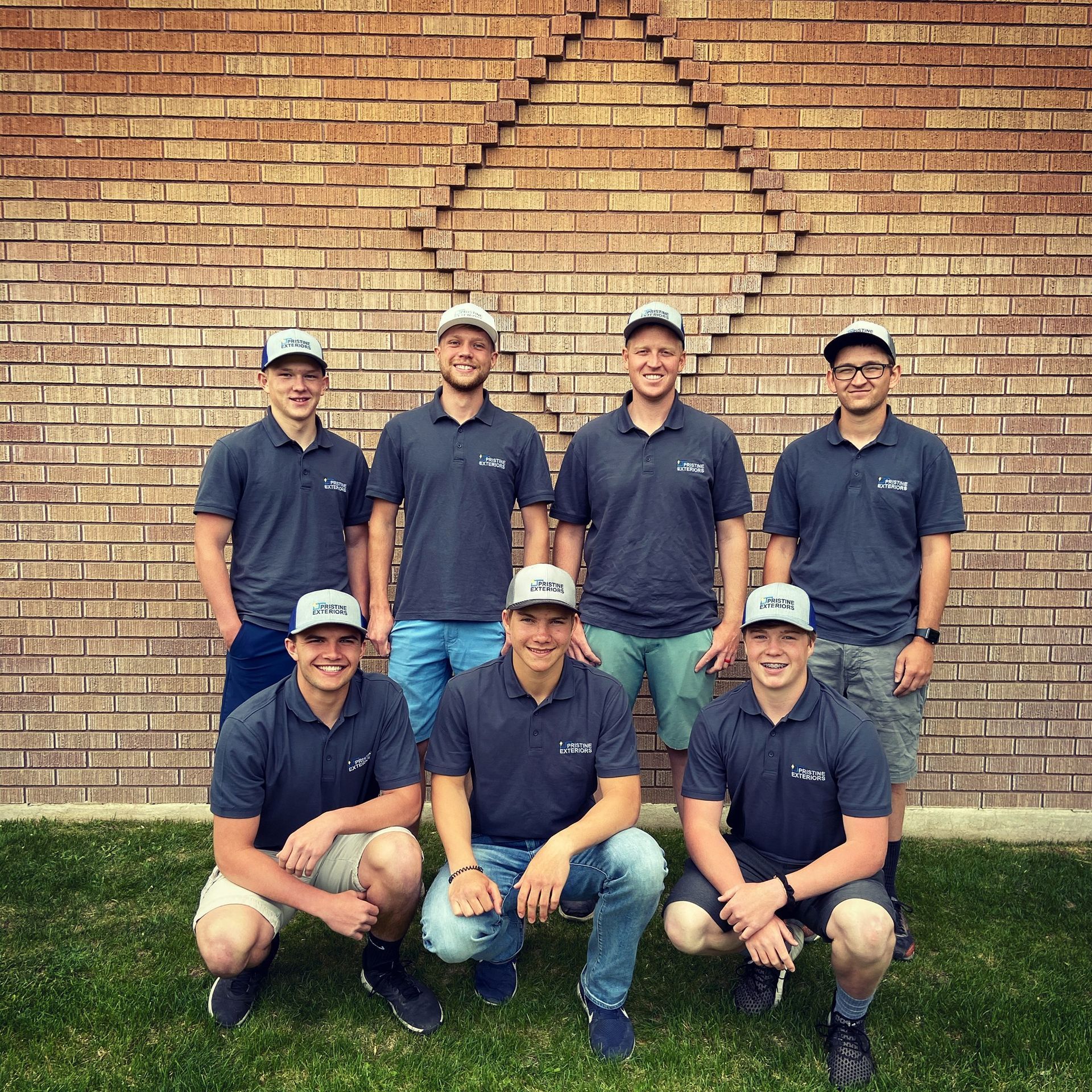 A group of men are posing for a picture in front of a brick wall.