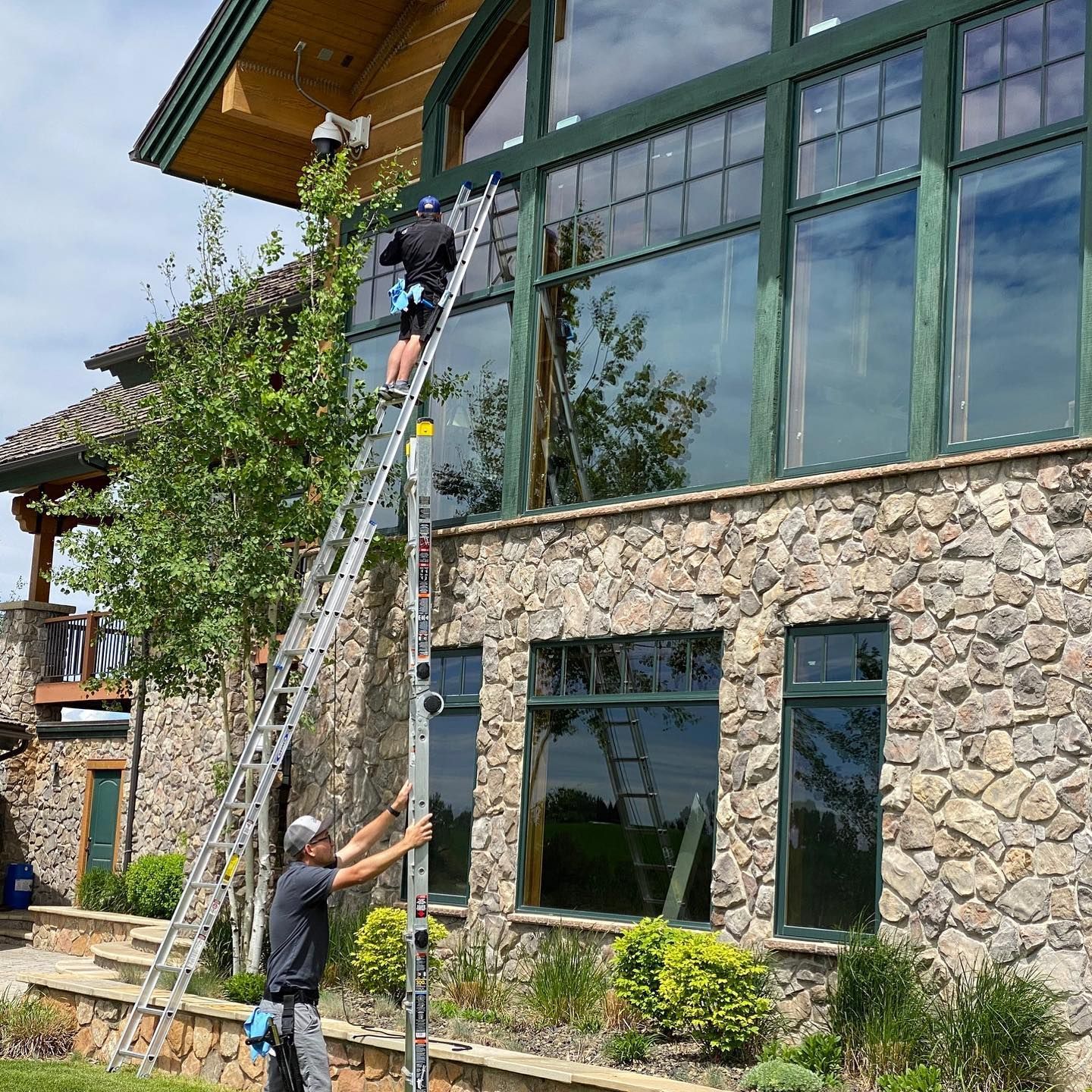 A man on a ladder is cleaning the windows of a large stone building.