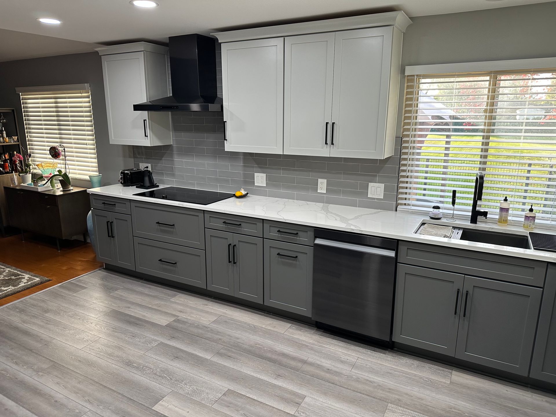 A kitchen with gray cabinets , white counter tops , stainless steel appliances and a sink.