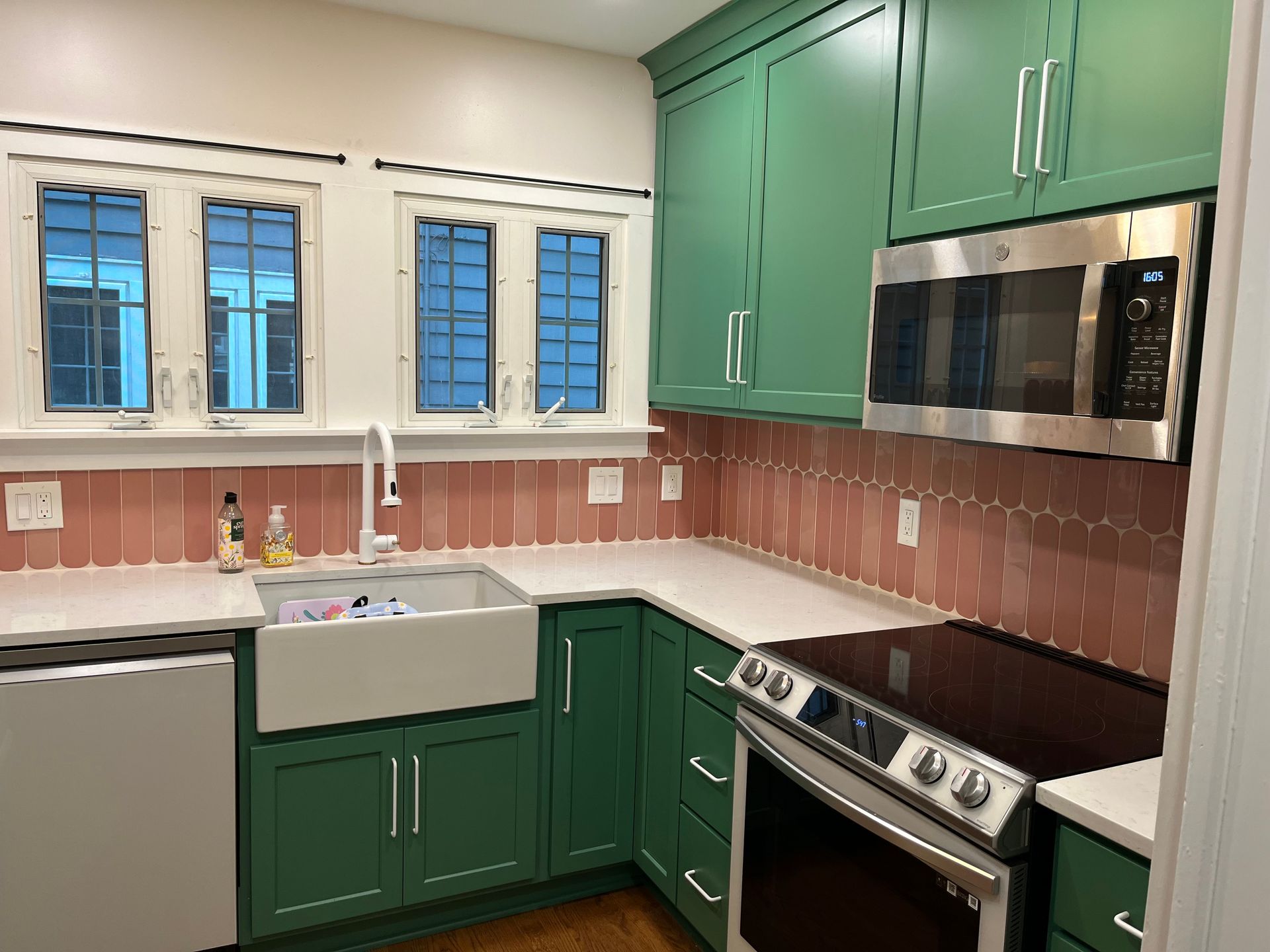 A kitchen with green cabinets , a stove , a sink , and a microwave.