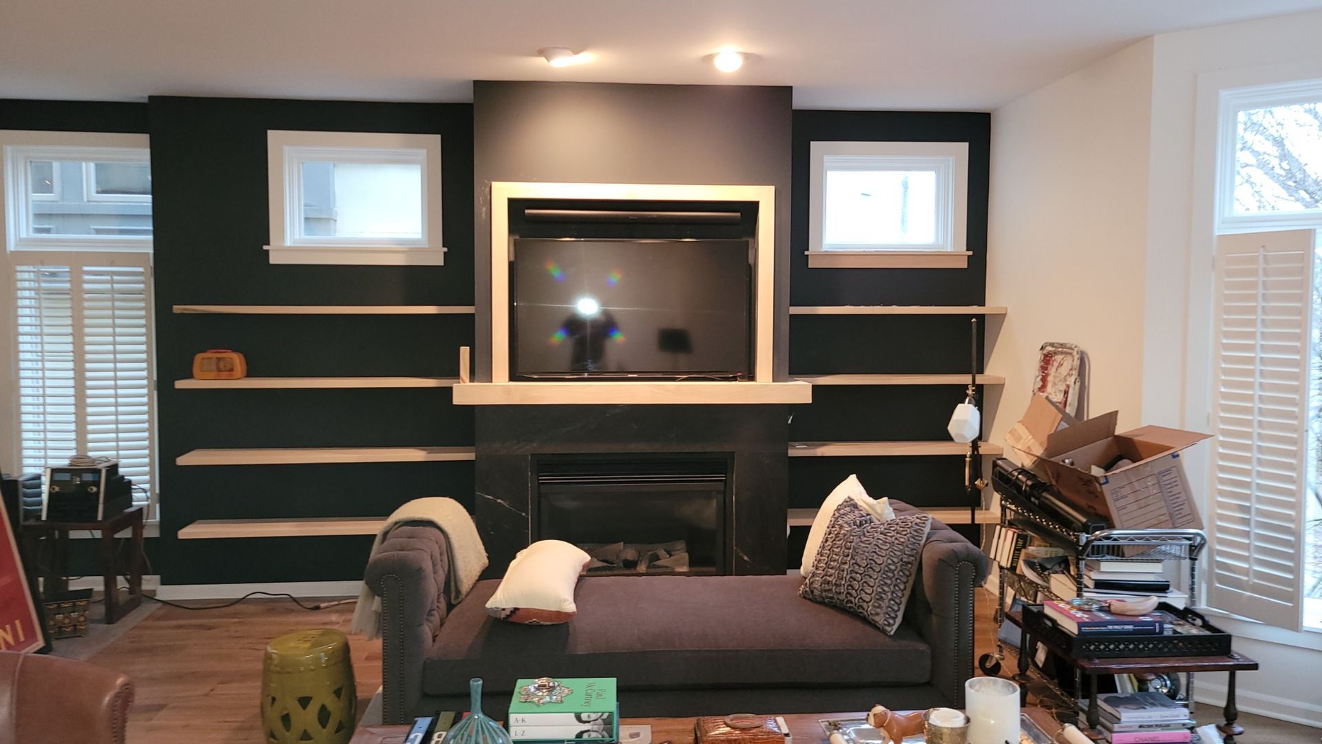 Living room with dark accent wall, shelves, fireplace, TV, chaise lounge, and windows.