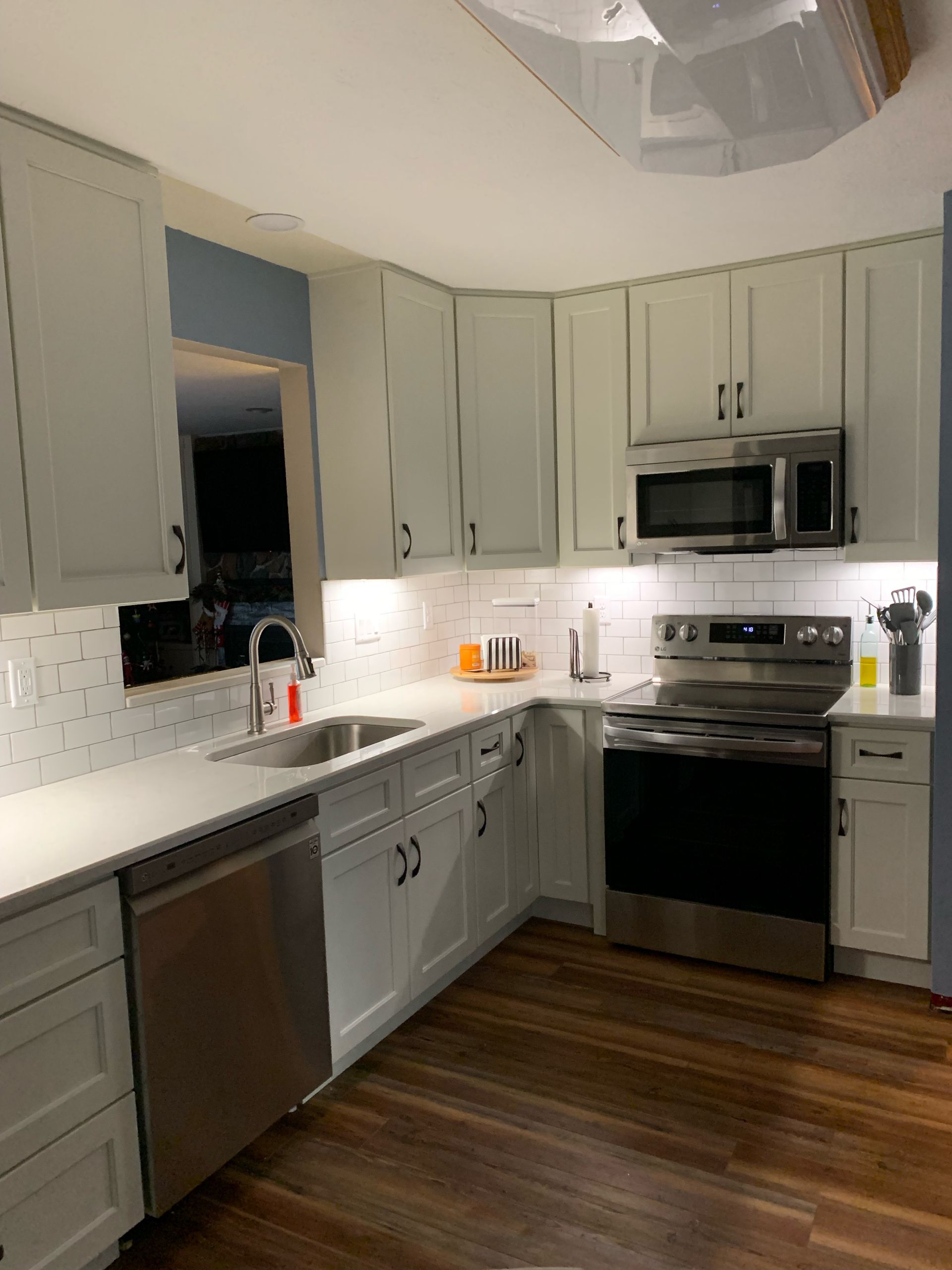 A kitchen with white cabinets , stainless steel appliances , a sink , and a microwave.