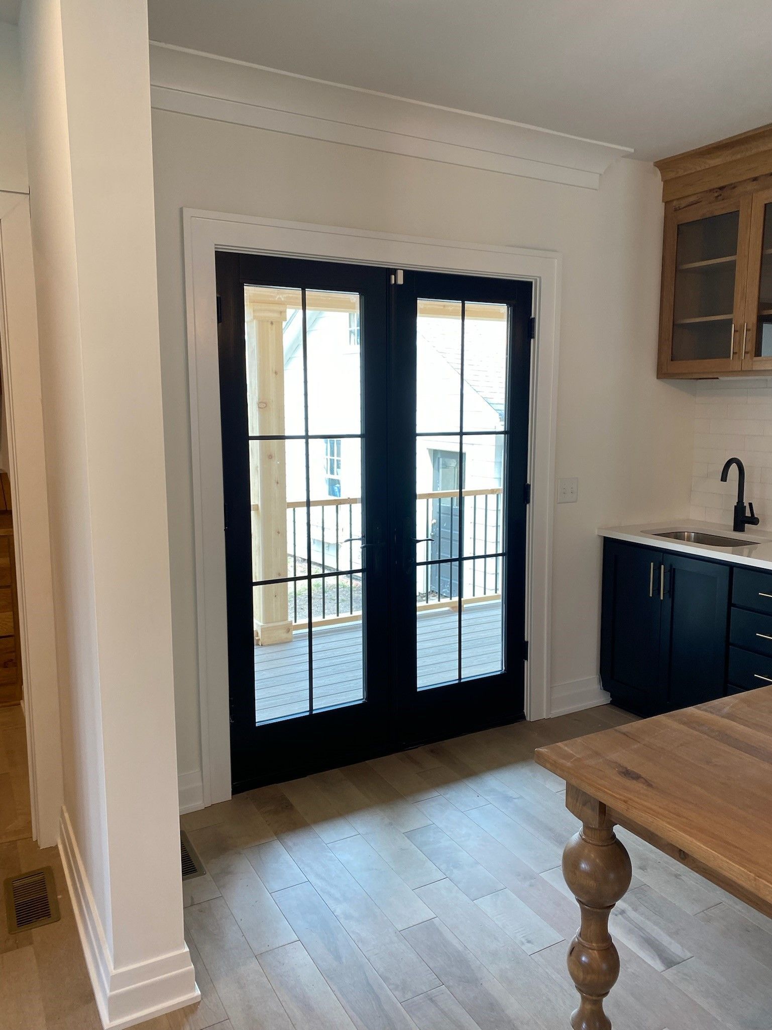 Black French doors framed by white trim, leading to a balcony. A dark blue cabinet and sink are visible.