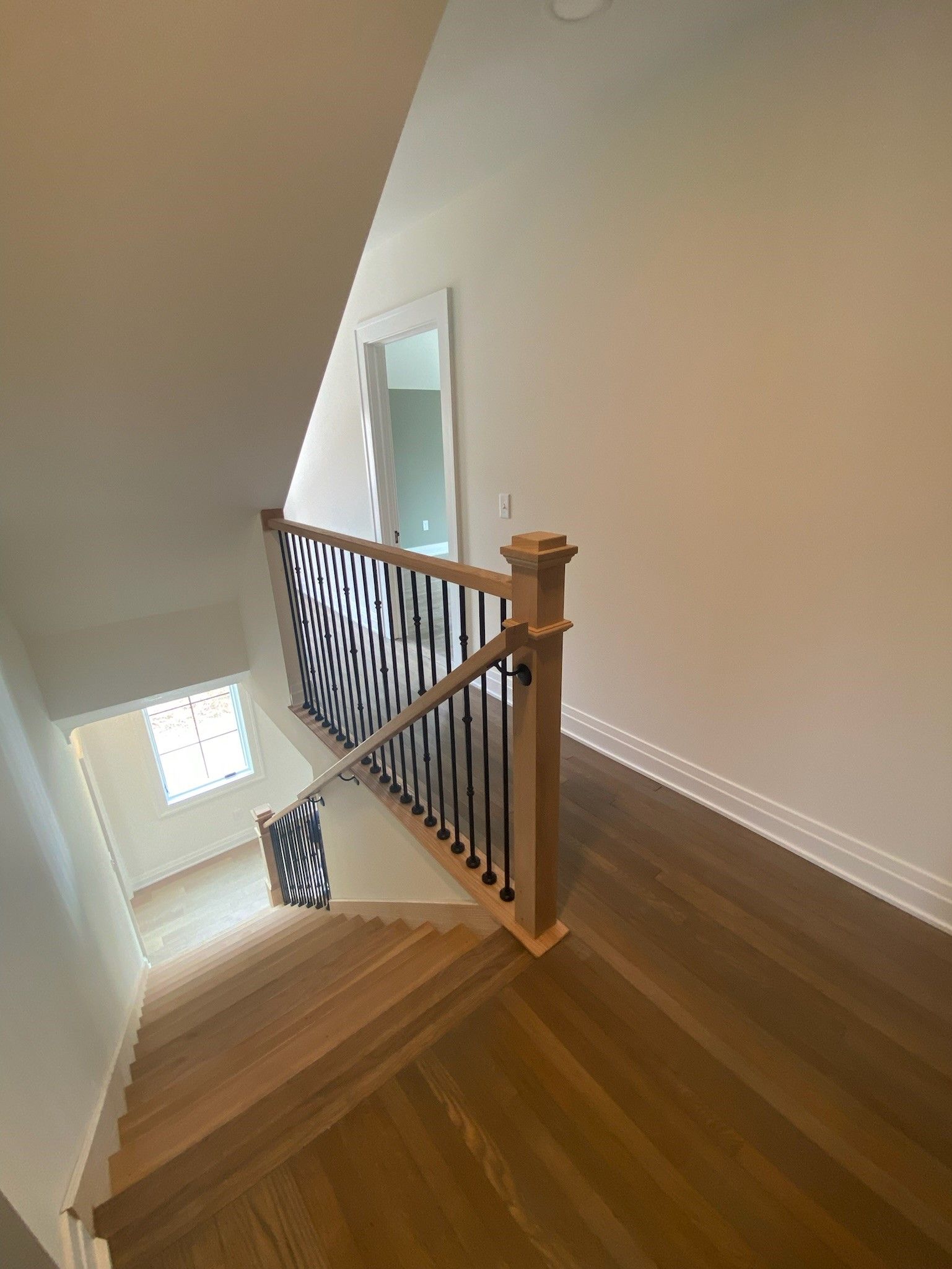 Staircase with wooden steps and railing, viewed from above. Beige walls, light wood floors.
