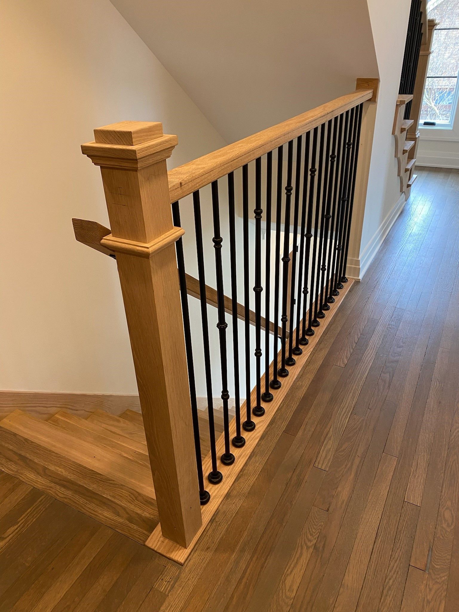 Wooden staircase with black metal spindles, next to a white wall.